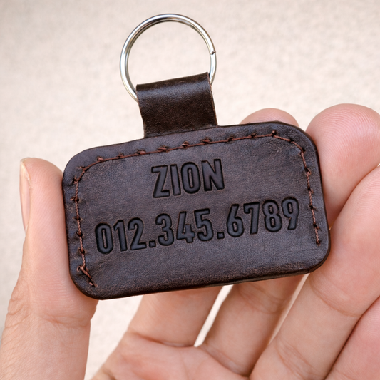 Handcrafted custom dog ID tag, back view showing engraved name and phone number on leather with key ring