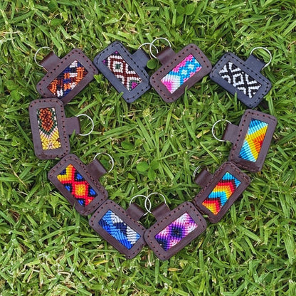 Handcrafted custom dog ID tags in assorted woven patterns, leather trim with key rings, flat lay arranged in a heart shape on grass